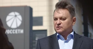 Чоловік у темному костюмі розмовляє біля вивіски компанії Россети